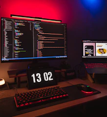 A high-performance desktop computer setup with colorful LED lighting and multiple monitors displaying code and graphics.