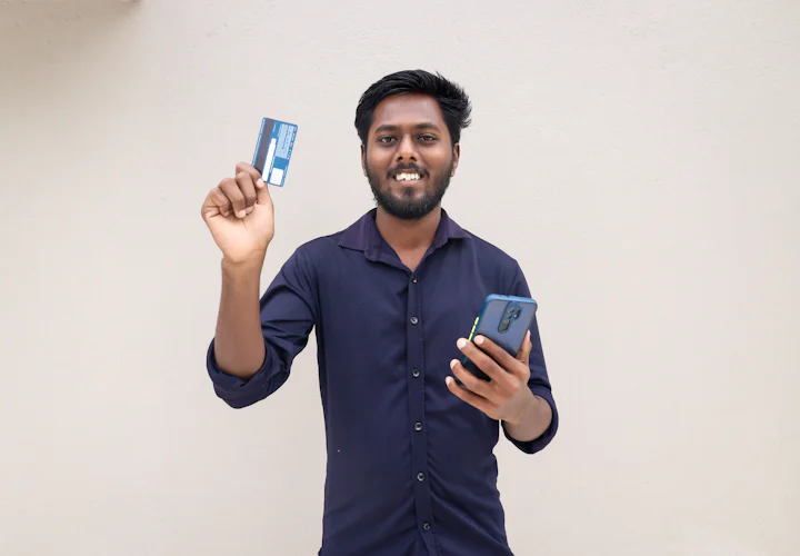 A smiling man holding a card and a phone, ready to pay