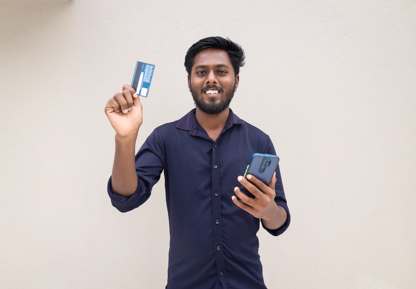 A smiling man holding up a payment card and a smartphone