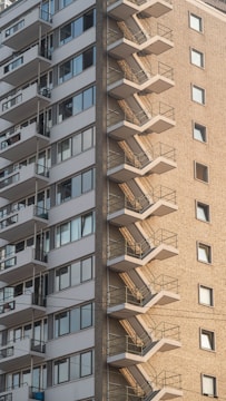 A tall residential building with a prominent external staircase running along the side. The facade features a mix of brick and concrete with numerous windows, some with balconies.