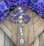 Purple rosary beads are placed on a wooden surface, surrounded by vibrant purple flowers. The rosary features silver medallions and a larger medallion at the end with religious imagery.