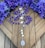 Purple rosary beads are placed on a wooden surface, surrounded by vibrant purple flowers. The rosary features silver medallions and a larger medallion at the end with religious imagery.