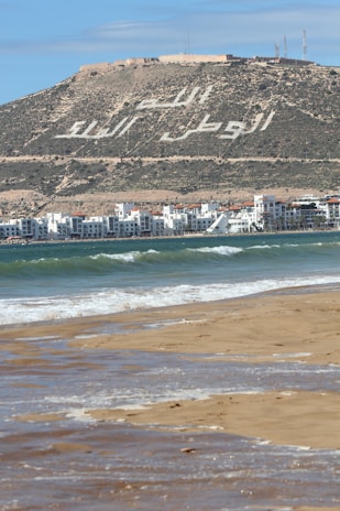a beach with buildings and a hill in the background