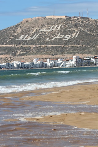a beach with buildings and a hill in the background