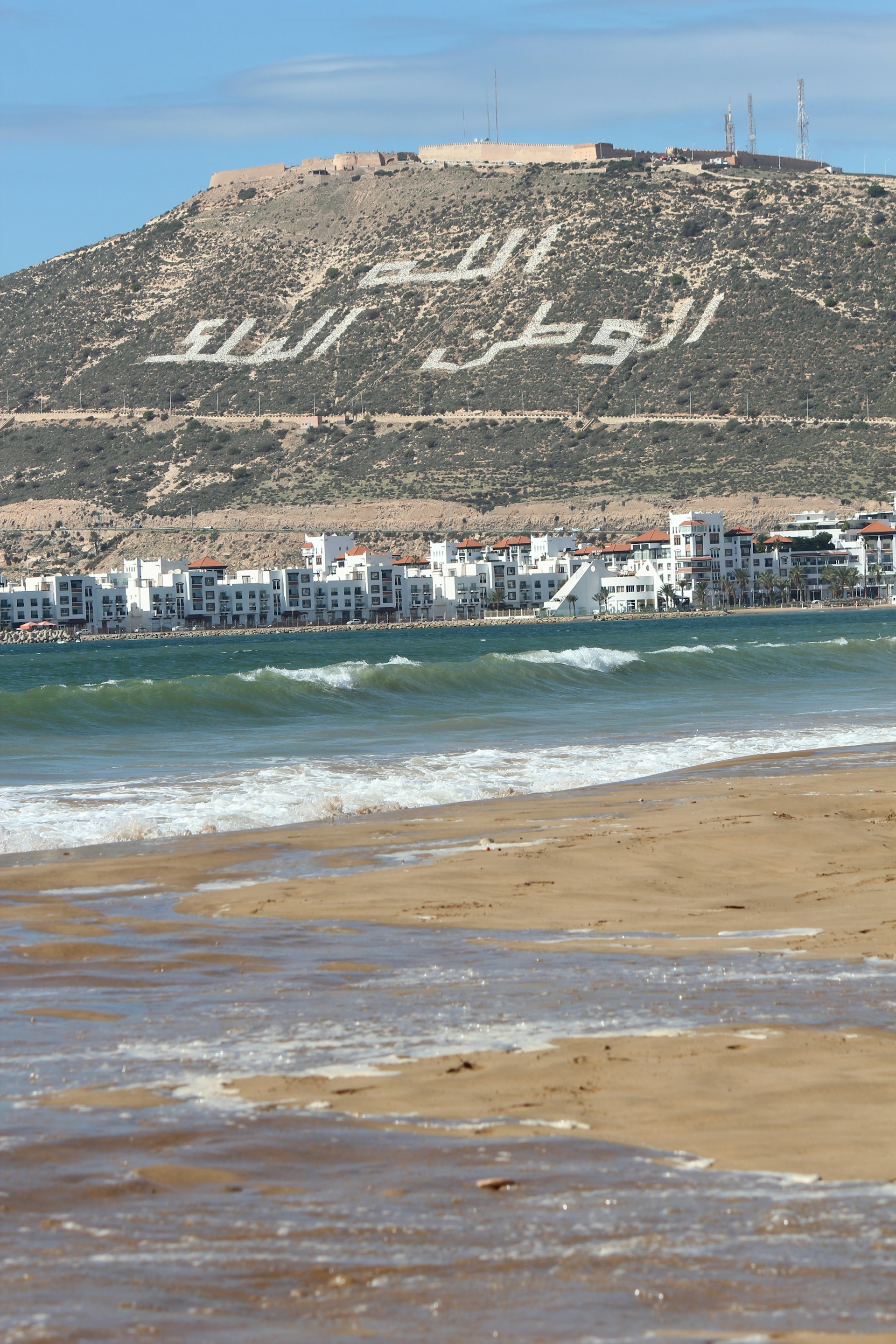 a beach with buildings and a hill in the background
