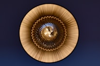 A circular, symmetrical pattern with a glass or metallic texture, featuring ridged, radial lines emanating from the center. The design creates a sense of depth and reflection with an intricate, geometric appearance.