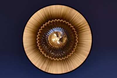 A circular, symmetrical pattern with a glass or metallic texture, featuring ridged, radial lines emanating from the center. The design creates a sense of depth and reflection with an intricate, geometric appearance.