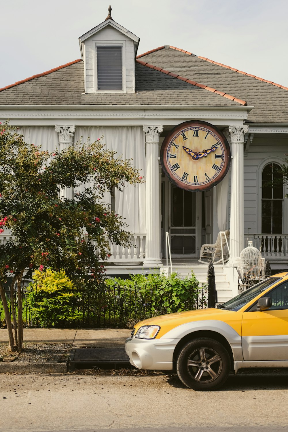 a yellow car parked in front of a white house with a clock