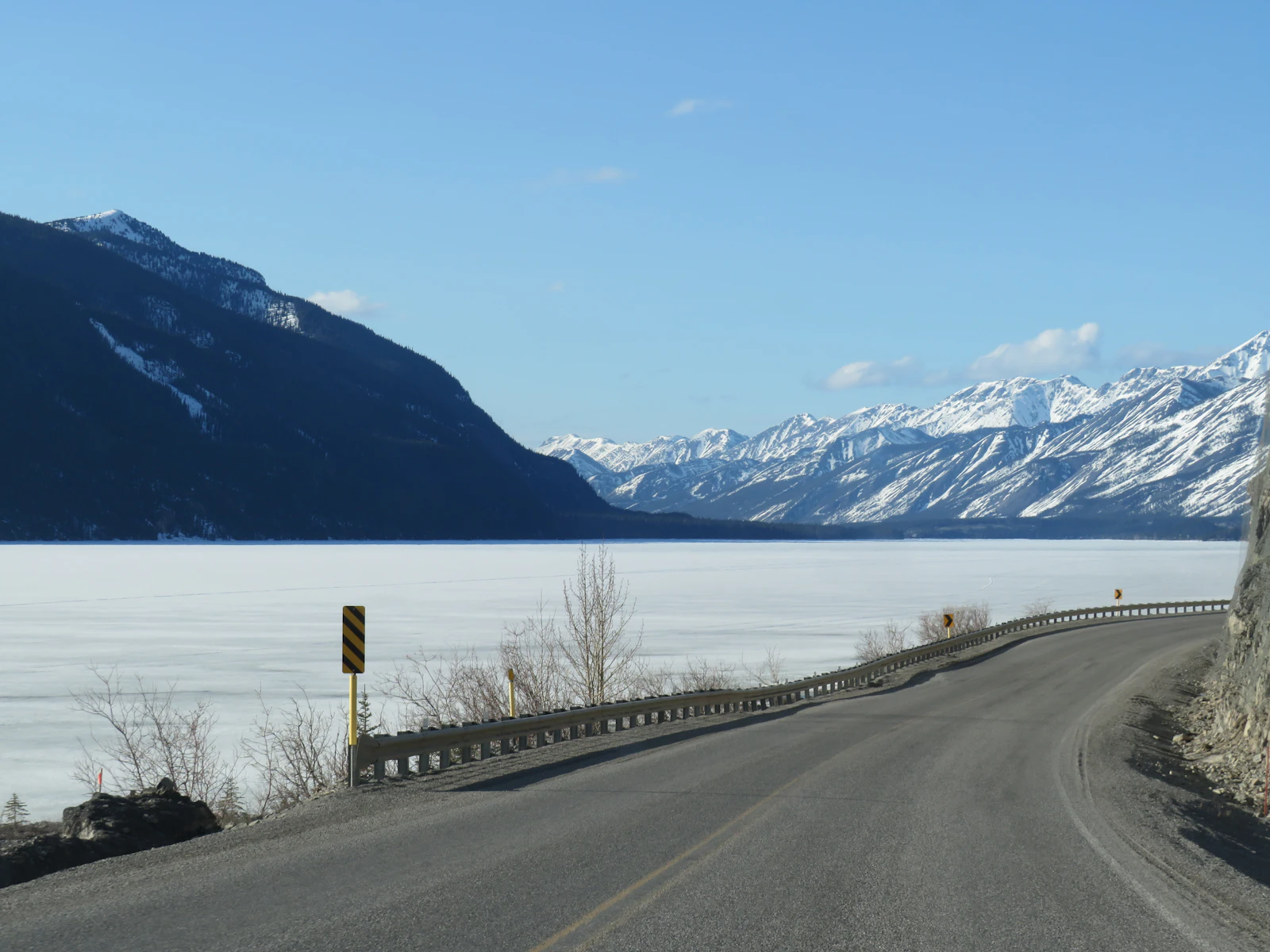 A highway curving beside a frozen inlet below snowy mountains