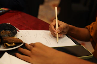 Close-up of a hand writing a message on a rustic wooden table with a brownie and coffee nearby