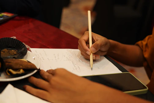 Close-up of a hand writing a message on a rustic wooden table with a brownie and coffee nearby