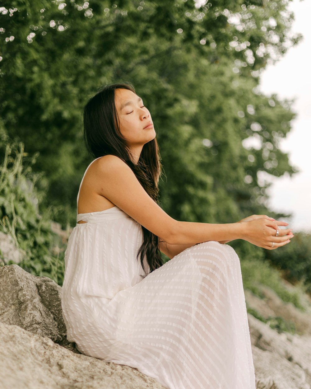 a woman in a white dress sitting on a rock