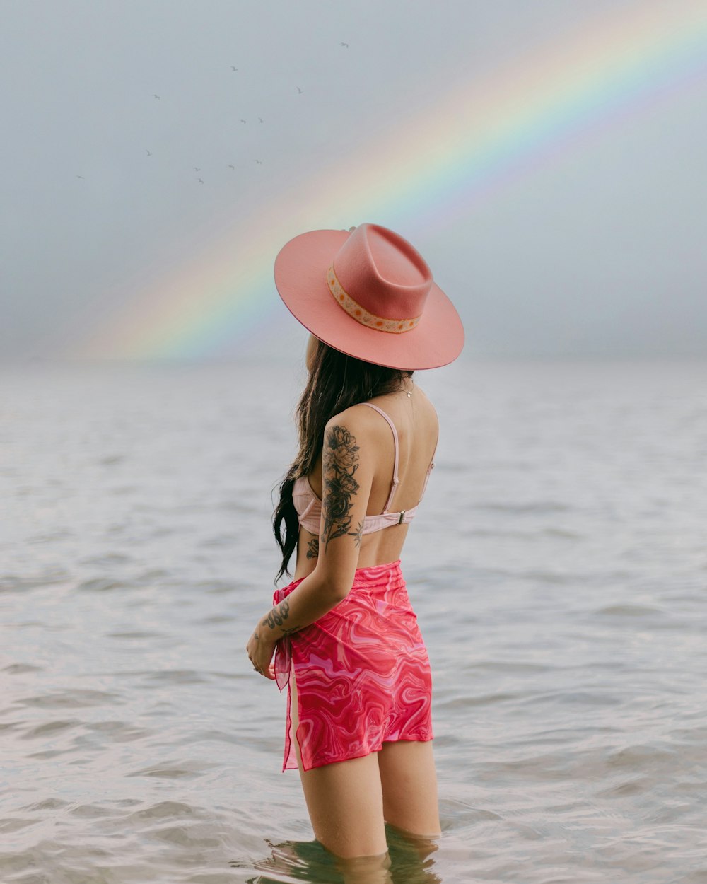 a woman in a garment and hat standing in water with a rainbow