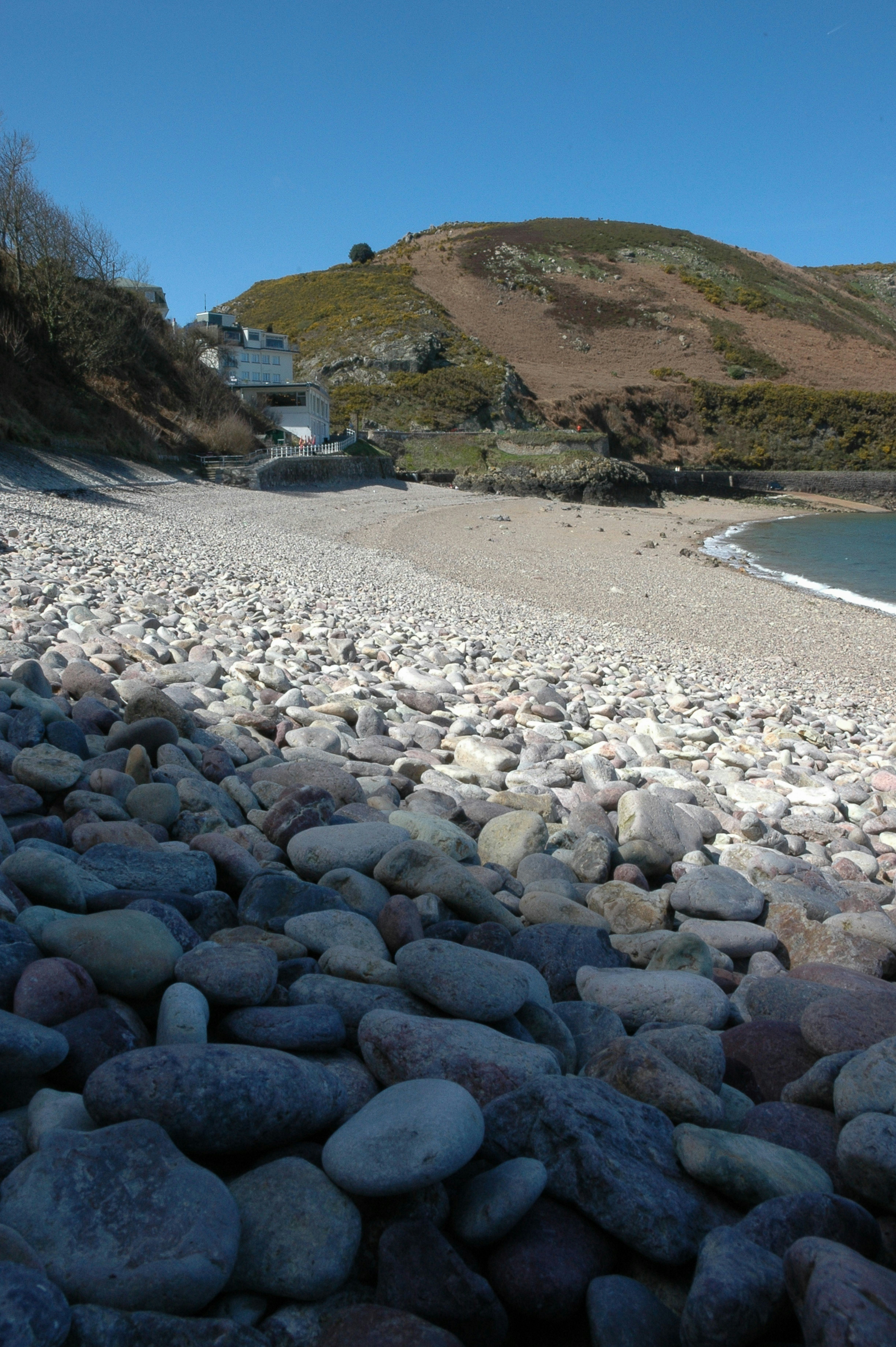 A rocky beach with a building in the distance photo – Free Trinity ...