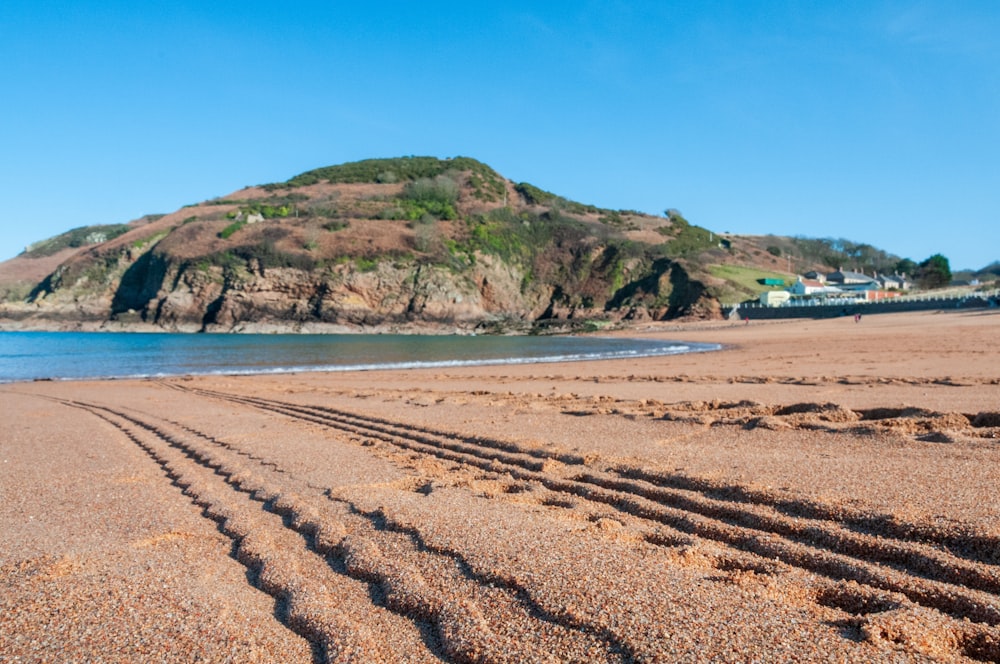 a sandy beach with a hill and buildings in the background