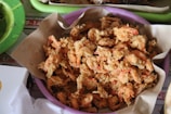 A bowl filled with crispy, fried shrimp, presented on a piece of brown paper which lies on a purple tray. The shrimp have a golden, crunchy batter and are placed in a casual, informal setting.