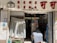 A small convenience store entrance with a curtain partially covering the doorway. The store has a variety of goods including bottled water, drinks, and household items. The signage above the entrance includes both Chinese characters and English text.