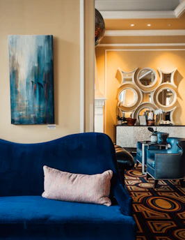 A sleek, modern living room showcasing a luxurious royal blue velvet sofa with golden accents under soft ambient lighting.