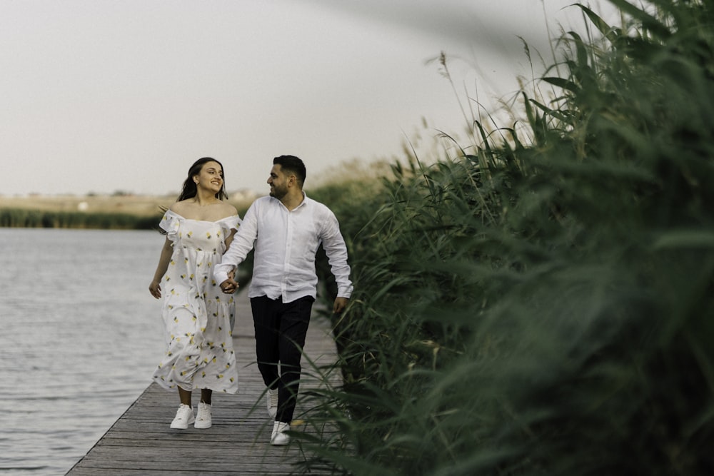 a man and woman walking on a dock by water