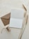 An open blank card and a brown envelope are placed on a textured surface alongside a spool of string and three stalks of wheat.