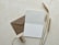 An open blank card is placed next to a brown envelope. Three wheat stalks and a spool of string with twine wound around it are positioned nearby on a textured, light-colored surface.