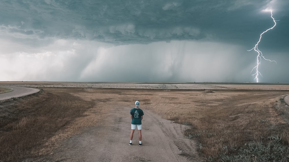 a person standing on a dirt road with lightning striking the ground
