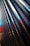 A close-up of a metallic surface with a series of round perforations, creating a repetitive pattern. The surface reflects light with shades of blue, red, and white creating a dynamic visual effect.