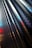 A close-up of a metallic surface with a series of round perforations, creating a repetitive pattern. The surface reflects light with shades of blue, red, and white creating a dynamic visual effect.