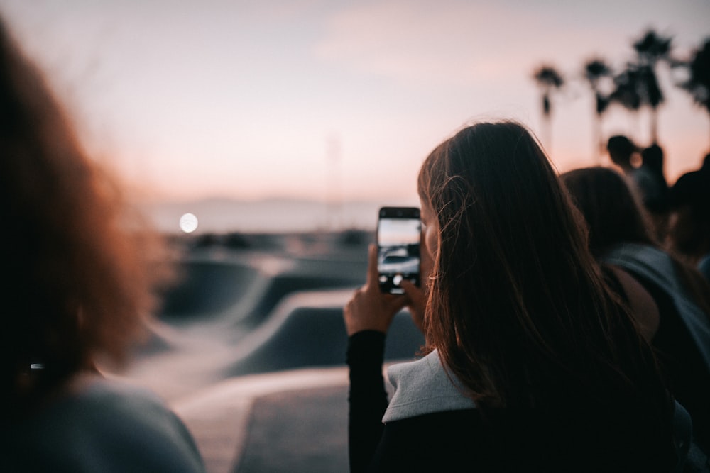 a woman taking a picture of a sunset