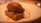 A rich dessert featuring a dark chocolate ice cream scoop placed on a rectangular piece of cake with nuts and caramel. Accompanied by a dollop of cream, the dessert is artfully arranged on a white plate with warm lighting.