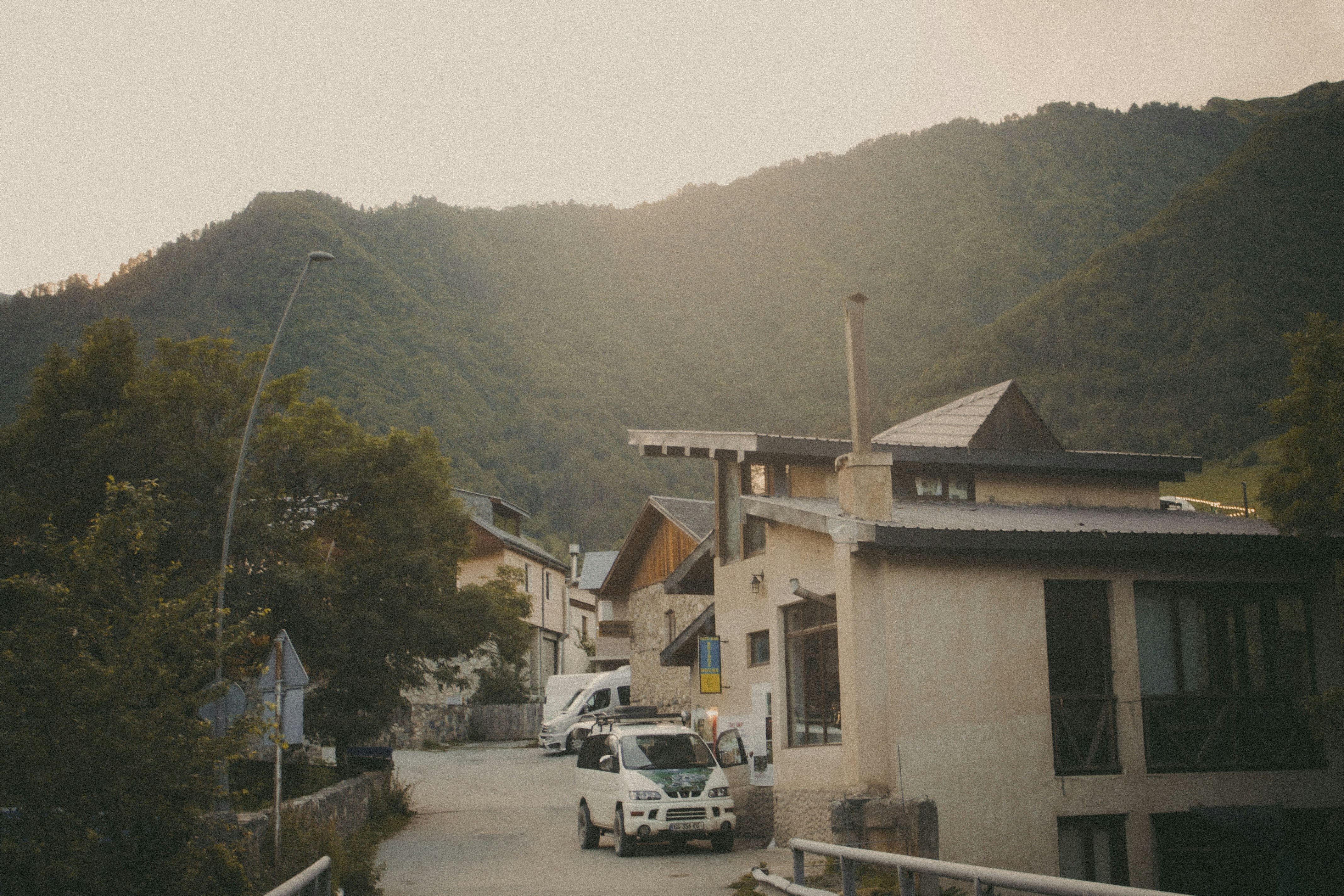 a street with cars and trees on the side and a building with mountains in the background