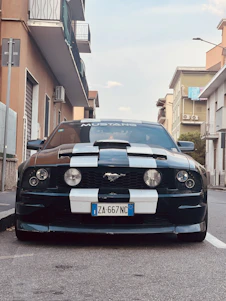 Close-up shot of a sleek black Ford Mustang featuring an aggressive front splitter and widebody kit under moody urban lighting.