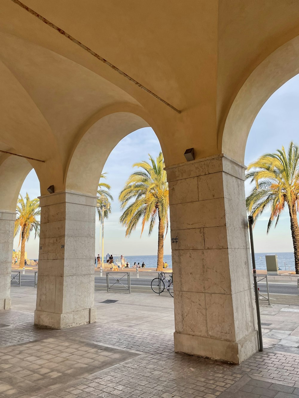 a stone walkway with pillars and palm trees