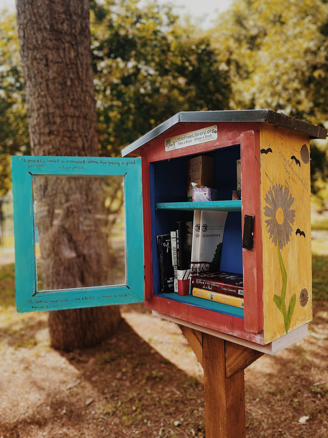 A brightly painted little free library with its door open, books inside