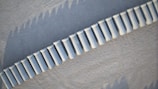 Aerial view of a series of white cylindrical concrete barriers placed in a curved line on a textured gray surface.