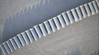 Aerial view of a series of white cylindrical concrete barriers placed in a curved line on a textured gray surface.