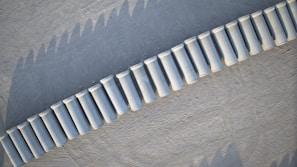 Aerial view of a series of white cylindrical concrete barriers placed in a curved line on a textured gray surface.