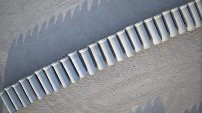 Aerial view of a series of white cylindrical concrete barriers placed in a curved line on a textured gray surface.