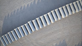 Aerial view of a series of white cylindrical concrete barriers placed in a curved line on a textured gray surface.