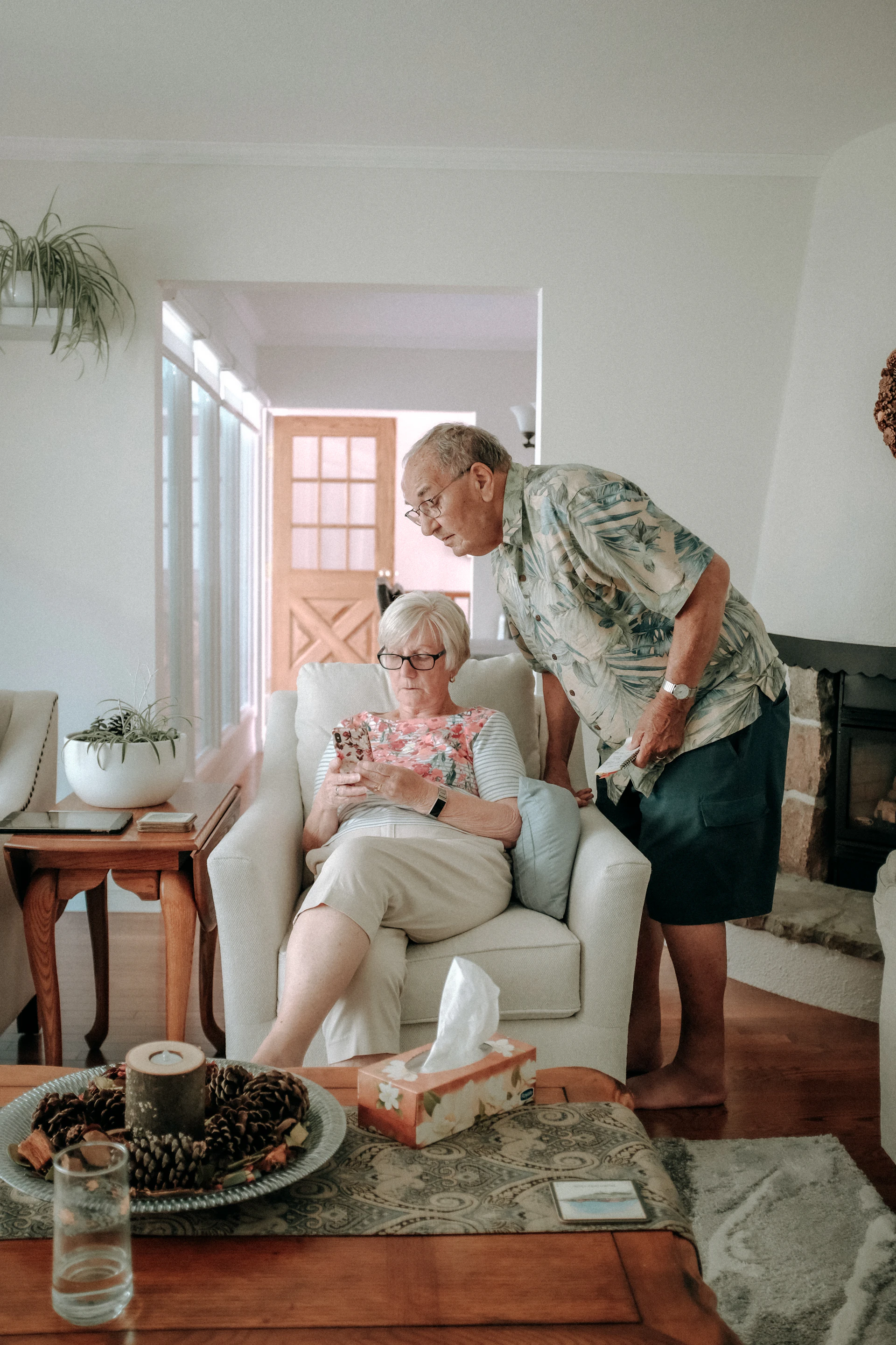 A smiling caregiver sitting with an elderly woman, sharing a tablet and a warm cup of tea