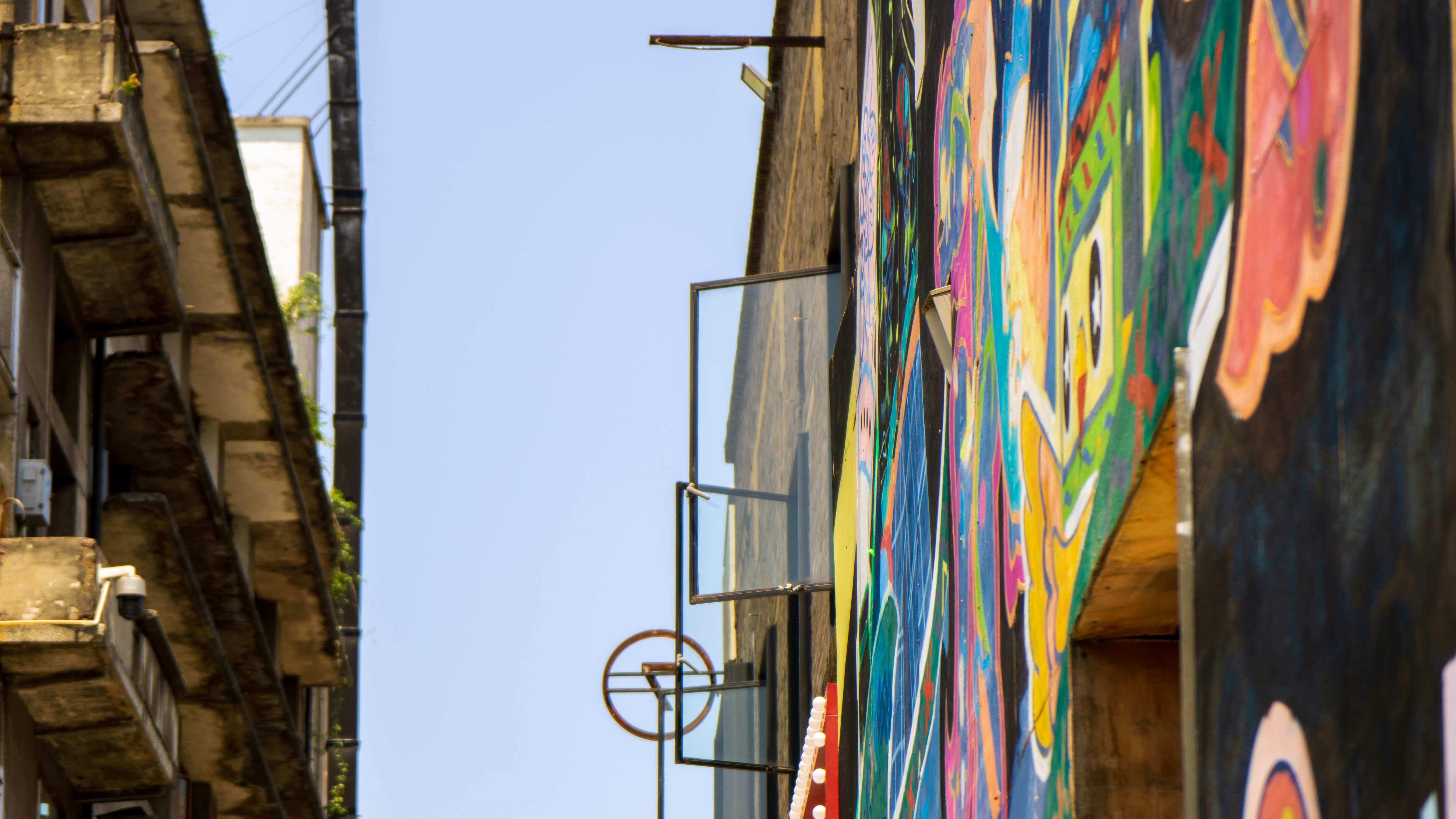 a street with a wall of colorful flags, A window on the colourful wall open.