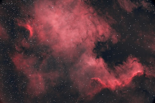 A stunning cosmic scene featuring a nebula with vibrant pink and red hues swirling amidst the vastness of space. The background is dotted with numerous stars, adding a sense of depth and mystery. Dark regions interlace with the brighter portions, creating a dramatic contrast.
