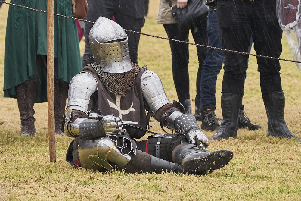 a person in armor kneeling on the ground with another man in the background