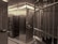 An interior space dominated by metal surfaces and structures, resembling a vault or secure facility. The walls and door are made of metal, with visible rivets and steel bars forming a secure area. There are numbered boxes on the left, possibly indicating storage or safety deposit boxes, and a shelf with a small object or item placed on it.