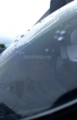 Close-up of a matte black Porsche 911's headlight with reflections.
