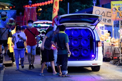 A sleek audio system setup illuminating a bustling outdoor market at dusk, highlighting the clear speakers and wiring.