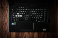 A black laptop keyboard with highlighted W, A, S, D keys, set against a wooden surface. The stickers indicate Intel Core i7 and NVIDIA GeForce GTX components.
