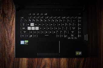 A black laptop keyboard with highlighted W, A, S, D keys, set against a wooden surface. The stickers indicate Intel Core i7 and NVIDIA GeForce GTX components.