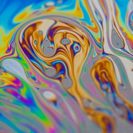 A mesmerizing swirl of vibrant colors creating abstract patterns reminiscent of a psychedelic art piece. The image features an intricate blend of blues, yellows, purples, and oranges with bubble-like formations and flowing lines.