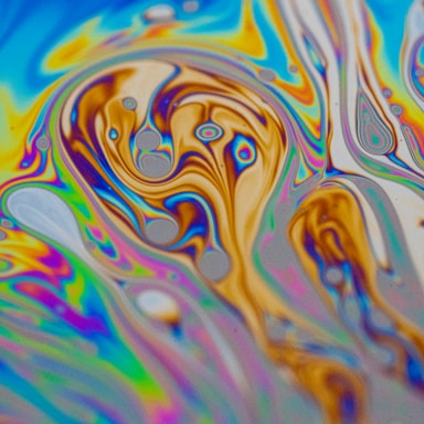 A mesmerizing swirl of vibrant colors creating abstract patterns reminiscent of a psychedelic art piece. The image features an intricate blend of blues, yellows, purples, and oranges with bubble-like formations and flowing lines.